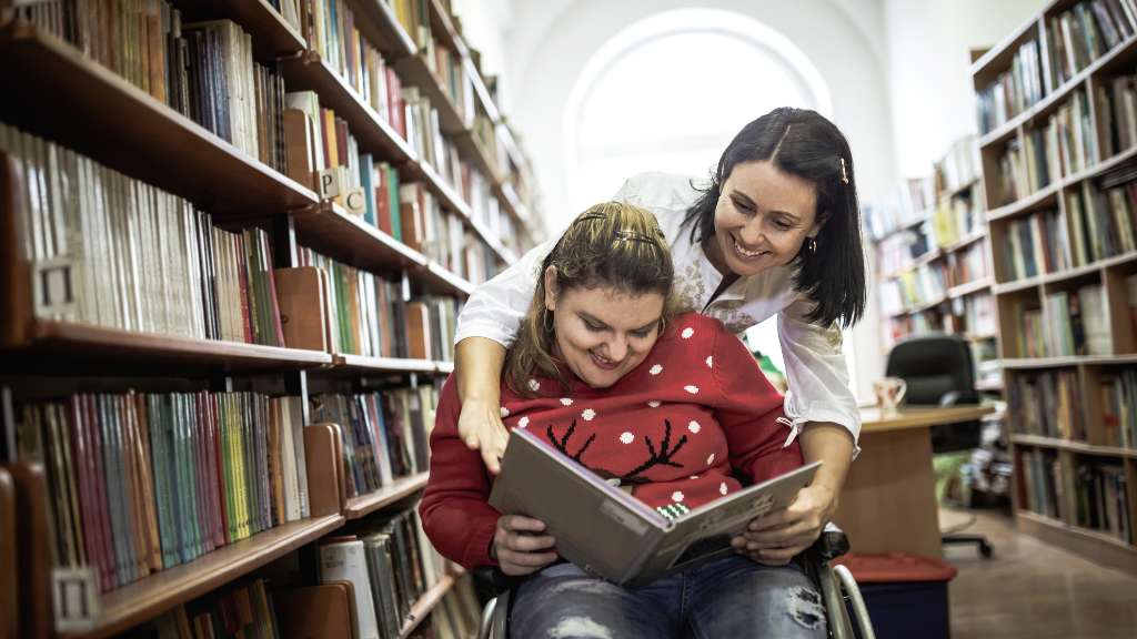A person in a wheelchair reading a book in a library.