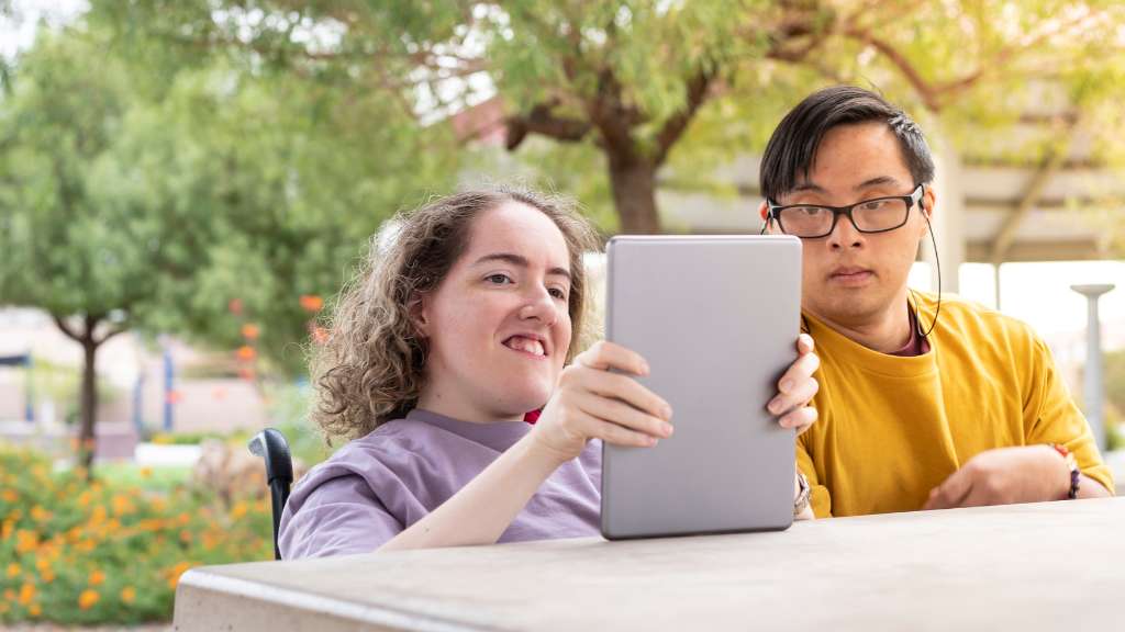Two disabled people view a tablet display. Website accessibility is helping for those with disabilities and improves overall user experience.